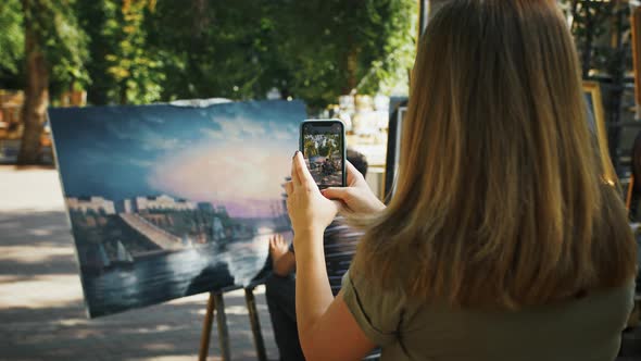 Unknown Female Taking Photos on Cellphone of Male Artist Who Drawing a Picture