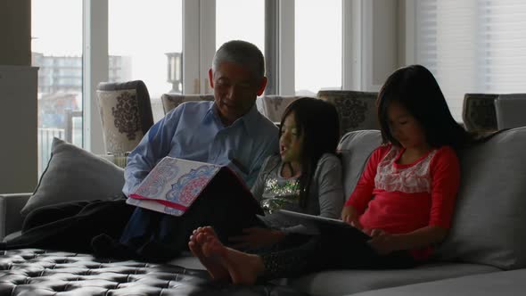 Front view of old senior asian grandfather and cute granddaughters using digital tablet at home 4k
