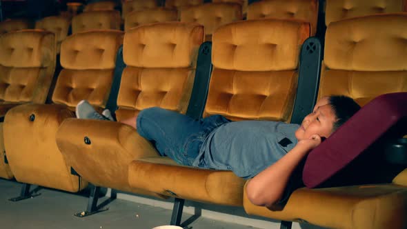 A Boy Laying Down on Armchair in Cinema