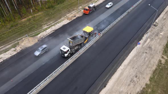 Road paver finisher working in tandem with truck. Hot asphalt for highway repair