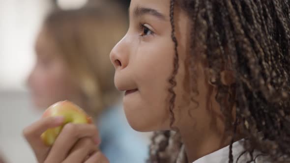 Side View Closeup of Happy Beautiful African American Girl Eating Healthful Apple with Blurred