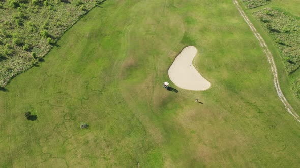 Man Plays Golf Near Cart on Green Course at Rural Site