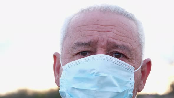 An Elderly Man in a Medical Mask Looks at the Camera