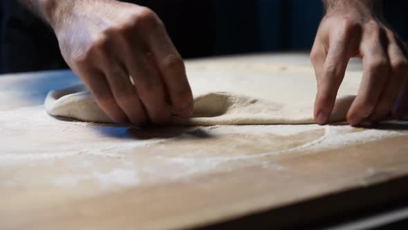 A close-up of a skilled chef's hands put pizza dough on the wooden counter, shallowing it and set it