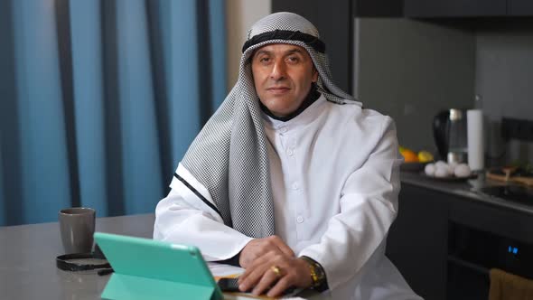 Portrait of Confident Middle Eastern Freelancer in Dishdasha and Chequered Keffiyeh Posing in Home