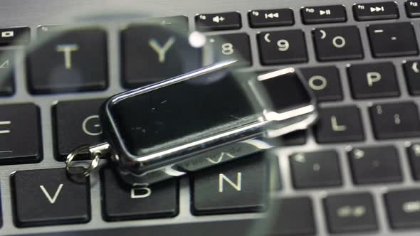 Hand holding a magnifying glass inspecting, examining an usb flash drive, memory stick, closeup