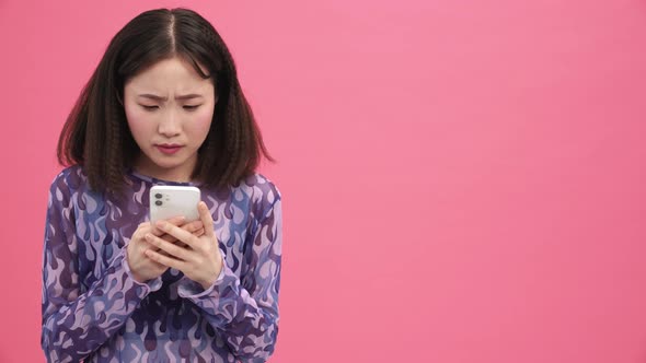 Displeased Asian woman typing on mobile