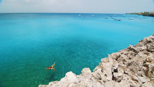 Young woman swimming to rocky cliff in vibrant Caribbean Sea in Curacao, SLOWMO