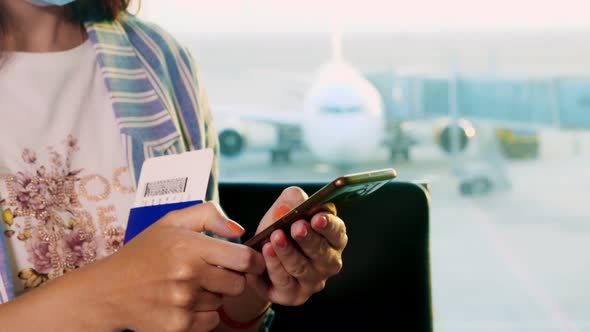 Close-up, Woman in Mask, with Passports and Tickets, Uses Mobile, Sitting in Front of Panoramic