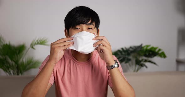 Man wearing face mask sits on couch in living room.