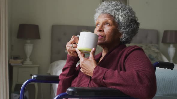Senior african american woman sitting on the wheelchair drinking coffee at home