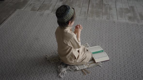 Little boy in prayer hat and arabic clothes with rosary beads and Koran book praying to God