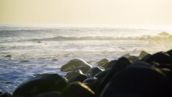 Waves crashing on rocks at sunrise golden hour