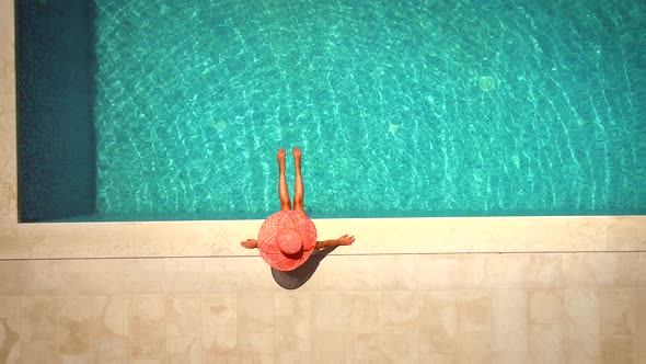 Aerial view of female with hat sitting by swimming pool.