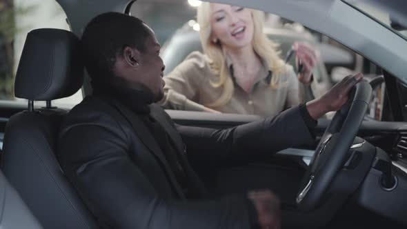 Blurred Caucasian Woman Giving Car Keys To the African American Man Sitting in Salon