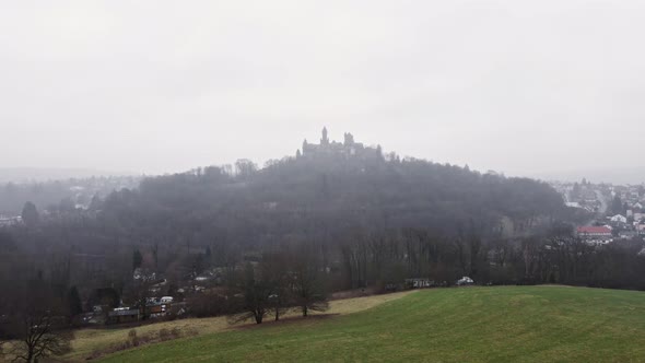 Braunfels Castle behind a green field on a cold and foggy winter day. Aerial tracking shot