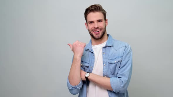 Young caucasian man smiling and pointing aside, showing something at blank space