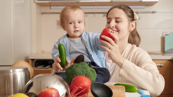 Smiling Mother with Baby Boy Playing and Singing Songs with Vegetables and Fruits on Kitchen