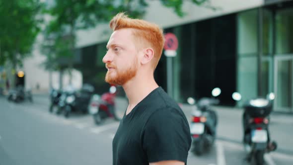 Serious red haired man walking in city