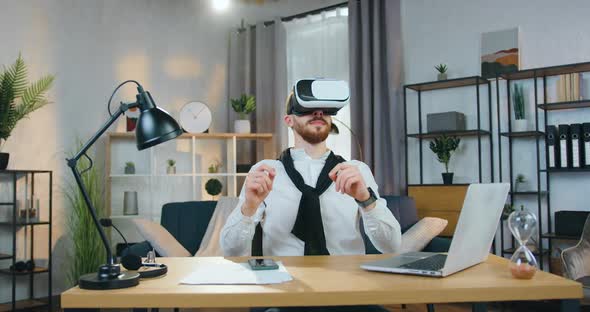 Man in Virtual Reality Headset Sitting at the Table in Home Office and Working on Imaginary Screen