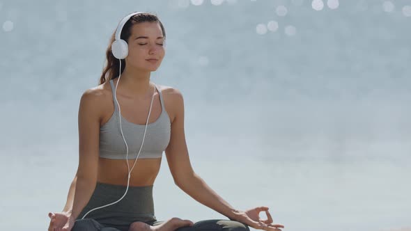 Woman in Yoga Meditation Pose with Headphones on the Beach