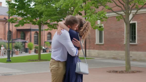 Side View of Young Couple Meet and Hug Outdoors on City Street