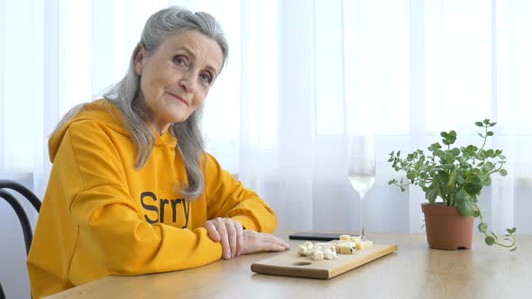 Beautiful Old Grandmother with Grey Hair and Face with Wrinkles Sitting at the Table at Home on