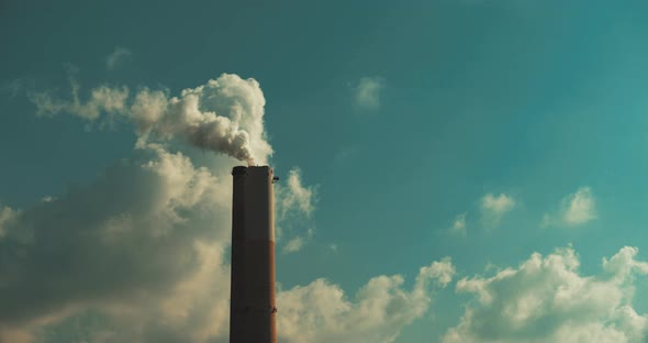 Smoke coming out of a coal power plant chimney against blue sky and clouds