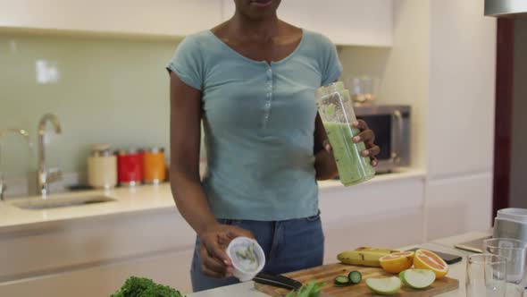 Smiling african american attractive woman tasting homemade smoothie in kitchen