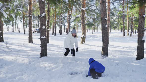 Mother and Son Plays with Snow in Winter Forest