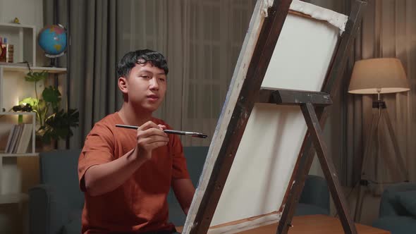 Asian Artist Boy Holding Paintbrush Mixed Colour And Thinking Before Painting On The Canvas