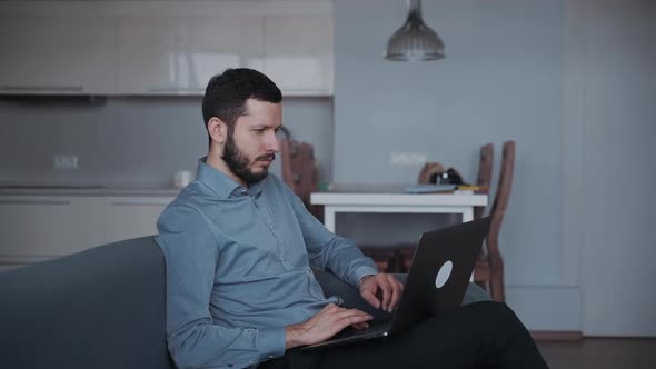 Man Using Modern Laptop and Sitting on Couch at Home