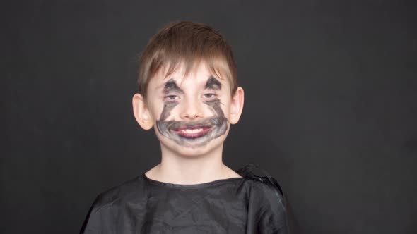 caucasian playful boy 8-9 years old in a black masquerade dress and make-up of a monster on the face