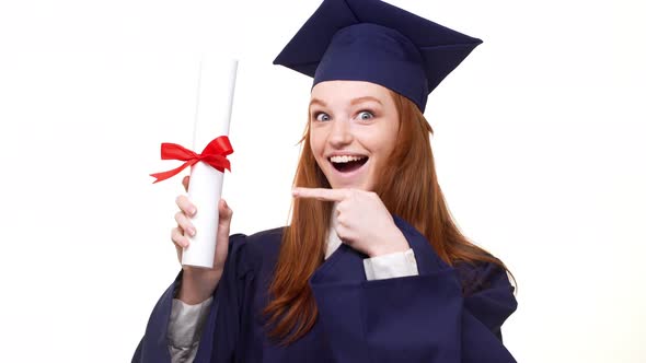 Exciting Caucasian Ginger Graduate Girl in Blue Robe and Square Academical Cap Showing Diploma