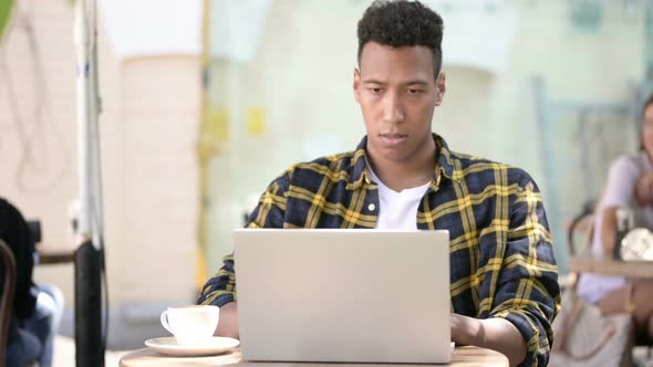 Young African Man Frustrated By Results on Laptop, Outdoor Cafe