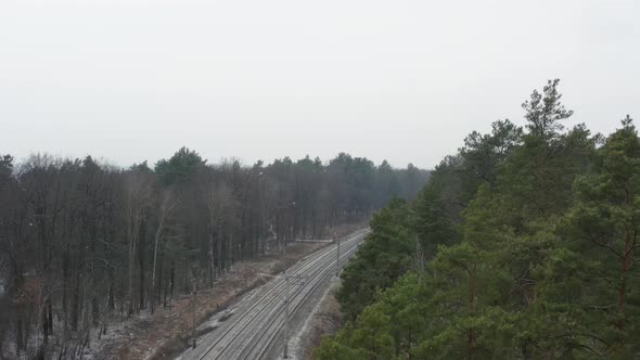 Aerial view of railway tracks in the forest during snowfall.
