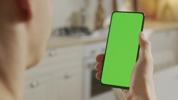 Back View of Man at Kitchen Room Sitting on a Chair Using Phone With Green Mockup Screen Chroma Key