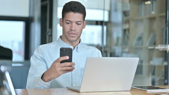 Young African Man Using Smartphone and Laptop