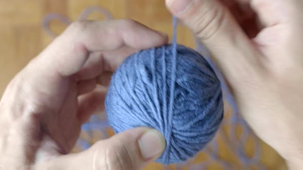 Close up of hand winding ball of blue wool. Blur background. Top view