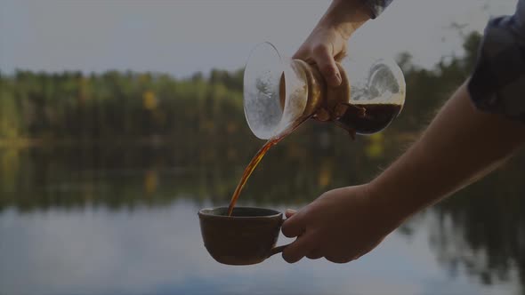 Pour over glass coffee maker, cafetiere pouring caffeine in a cup on a lake forest background