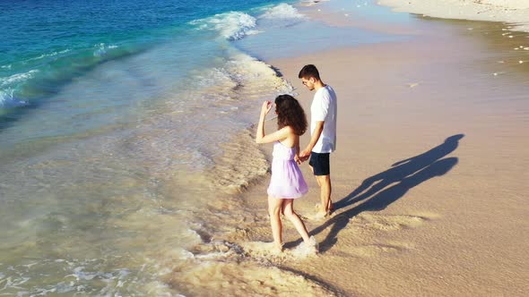 Young couple holding hands walking barefoot toward sea waves on exotic beach of tropical island, vac