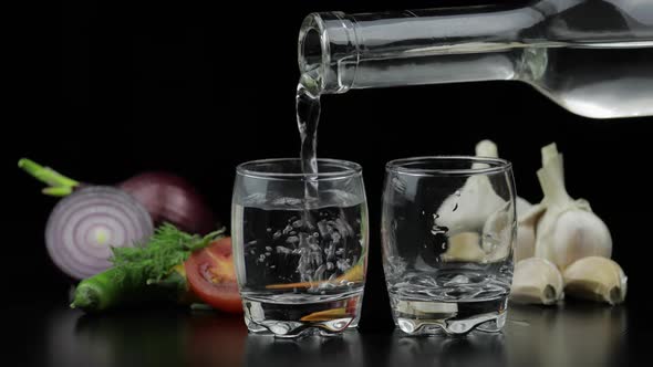 Pour Alcohol Vodka From a Bottle in Two Shot Glass. Background with Vegetables