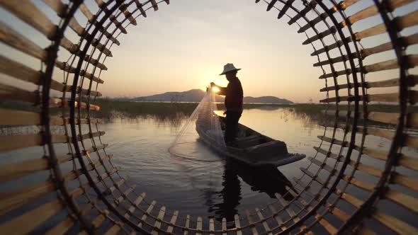 Silhouette fisherman throwing fishing net during sunset with boats at the lake.