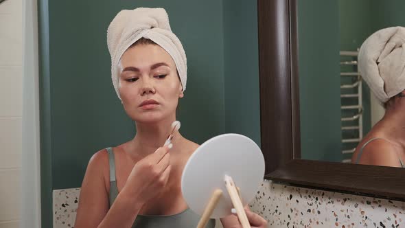 Young Woman Using Jade Facial Roller for Face Massage Sitting in Bathroom