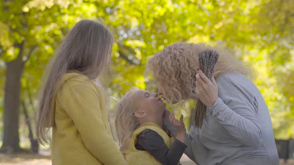 Portrait of Two Little Cute Caucasian Girls Kissing Their Mother