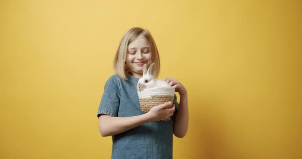 Teenager in a Blue Dress Holds a Basket with a Rabbit in Her Hand