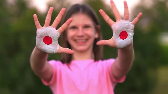 Happy Outdoor Portrait of Child Girl with Hands Painted in Japan Flag Colors