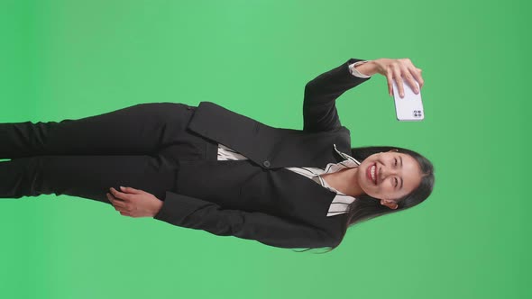 A Smiling Asian Business Woman Making Selfie On Mobile Phone On Green Screen In The Studio