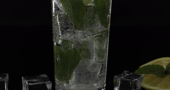 Clear Water in Glass with Green Mint Leaves and Ice Cubes on Black Background