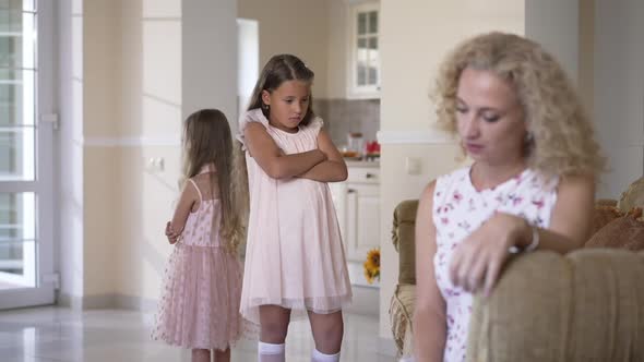 Stubborn Caucasian Little Sisters Standing with Crossed Hands Back to Back with Blurred Mother